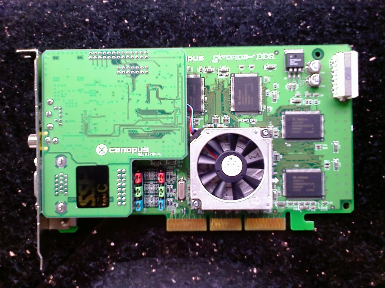 Canopus GeForce 256 DDR graphics card with green PCB, cooling fan, memory chips, and AGP edge connector
